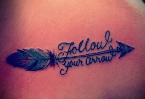 Фото тату: стрела с яркими перьями и надписью 'Follow your arrow'. Красивый рисунок татуировки для девушек, выполненный в цветном стиле.