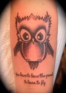 Фото тату мультяшной совы с большими глазами и надписью "You have to leave the ground to learn to fly".