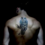 Фото минималистичной татуировки совы на спине. Черно-белый рисунок с акцентом на силуэт птицы.