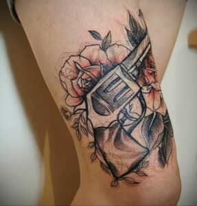 Фото тату револьвера, обвитого розами, выполненного в технике blackwork. Контрастный рисунок на ноге.