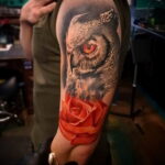 Фото тату совы с красной розой на руке. Цветная татуировка с реалистичной проработкой перьев и лепестков.