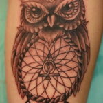 Фото тату совы в стиле blackwork, с детально проработанным ловцом снов и перьями, расположенной на руке.