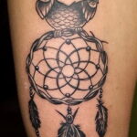 Фото татуировки совы, сидящей на ловце снов, выполненной в стиле blackwork с использованием плотных черных заливок и точечной техники.