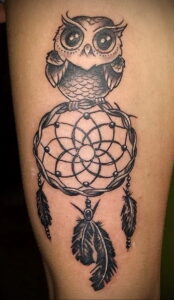 Фото татуировки совы, сидящей на ловце снов, выполненной в стиле blackwork с использованием плотных черных заливок и точечной техники.