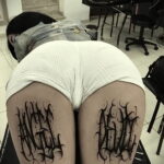 Фото тату: Две симметричные татуировки надписей, выполненные в стиле blackwork, расположены на ягодицах. Использованы плотные черные заливки и острые углы.