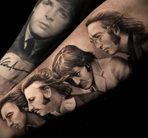 Фото тату на руке: реалистичные портреты участников группы The Beatles, выполненные в черно-серых тонах, с подписью.