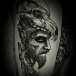 Фото тату в стиле blackwork, изображающее лицо воина с черепом, выполненное черными чернилами. Детализированная проработка линий и теней.