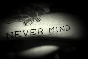 Фото тату минималистичной надписи 'Never Mind', выполненной черными чернилами на коже. Простой и лаконичный дизайн.