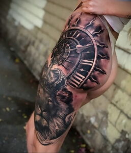 Фото тату на бедре с изображением волка, смотрящего на большие карманные часы. Символичный и детализированный рисунок, выполненный в реалистичном стиле.