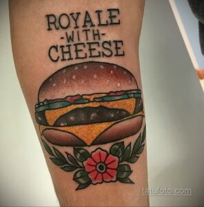 Фото тату на руке: бургер в стиле традишнл с надписью 'ROYALE -WITH- CHEESE' и красным цветком.