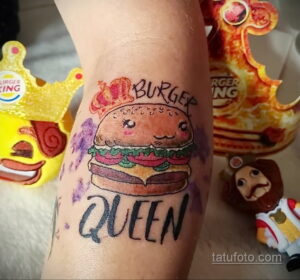 Фото татуировки с изображением бургера с надписью 'Burger Queen', выполненной в ярких цветах на руке.