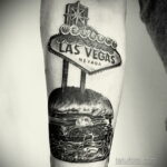 Фото тату реалистичного бургера на фоне вывески 'Welcome to Las Vegas'. Черно-белый рисунок, детализированный и атмосферный.