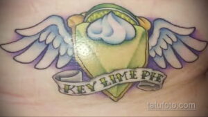 Фото тату на груди: пирог Key Lime Pie с крыльями и надписью. Яркие цвета, детализированная проработка и оригинальный сюжет.