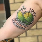 Фото тату на руке: половинка лайма с надписью 'Main Squeeze'. Яркие цвета, четкие контуры, традиционный стиль.