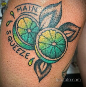 Фото тату двух долек лайма с надписью "Main Squeeze" и зелеными листьями. Цветной рисунок в стиле олдскул, расположенный на руке.
