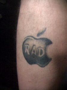Фото тату: Черно-серая татуировка логотипа Apple с надписью 'RAD' на предплечье. Простой и лаконичный рисунок татуировки.