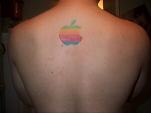 Фото татуировки на спине: логотип Apple, выполненный с использованием радужной цветовой палитры, символизирующий поддержку ЛГБТ.