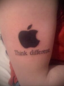 Фото тату на руке: логотип Apple и надпись 'Think different' в черном цвете.