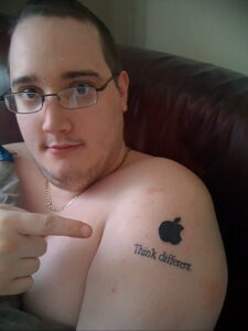 Фото тату: минималистичная татуировка логотипа Apple с надписью "Think different" на плече мужчины.