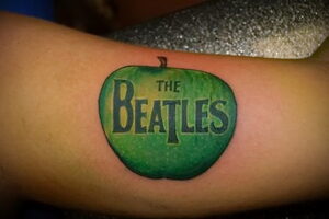 Фото тату на руке: зеленое яблоко с надписью 'The Beatles' внутри, выполненное в стиле ретро.