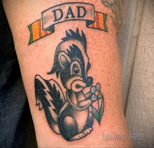 Фото тату: мультяшный хорек с цветком и надписью "DAD" в стиле олдскул на руке. Яркие цвета, четкие контуры.