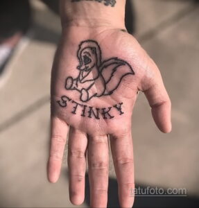 Фото миниатюрной татуировки скунса с надписью 'Stinky' на ладони. Небольшой и оригинальный дизайн.