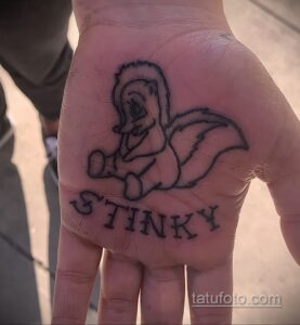 Фото миниатюрной татуировки скунса с надписью 'Stinky' на ладони. Небольшой и оригинальный дизайн.