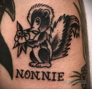 Фото татуировки сквонка, держащего цветок, с надписью "Nonnie". Черно-белый рисунок татуировки на руке, выполненный в стиле олд скул.