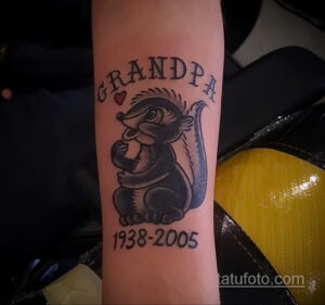 Фото тату скунса с надписью "Grandpa" и датами жизни. Черно-серый рисунок в минималистичном стиле.