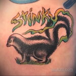 Фото тату скунса с надписью "Stink" над ним. Рисунок выполнен в ярких цветах с использованием градиентов и мультяшного стиля.