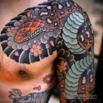 Фото тату на плече и груди с изображением змеи, обвивающейся вокруг цветущей сакуры. Яркий и детализированный рисунок татуировки в японском стиле.