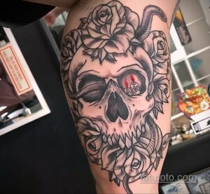 Фото тату в стиле blackwork с изображением черепа, увитого розами и обвитого змеей, на руке.