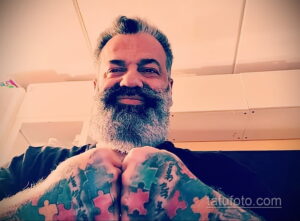 Фото мужчины с длинной бородой и татуировками в виде пазлов на руках и груди. Яркий пример самовыражения через искусство татуировки.