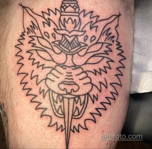 Фото тату волка с кинжалом в стиле blackwork на руке. Черно-белая татуировка с использованием плотной штриховки и геометрических элементов.