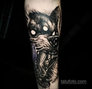 Фото тату зловещего волка на руке, выполненное в стиле dark art с использованием черного цвета и детализированной прорисовки. Рисунок татуировки демонстрирует агрессивный взгляд и острые клыки.