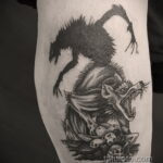 Фото тату волка на ноге, выполненное в стиле blackwork с использованием черных оттенков. Волк изображен на фоне черепов и костей.