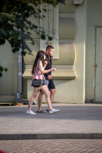 Фото тату: девушка с портретной татуировкой на плече и татуировкой на руке идет рядом с парнем. Современный городской стиль.