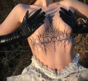 Фото татуировки в стиле blackwork, покрывающей грудь и живот. Изображены абстрактные узоры, напоминающие колючие растения и кресты. Татуировка выполнена черными чернилами.
