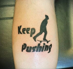 Фото тату с надписью 'Keep Pushing' и силуэтом скейтбордиста. Простая, но вдохновляющая татуировка в черном цвете.