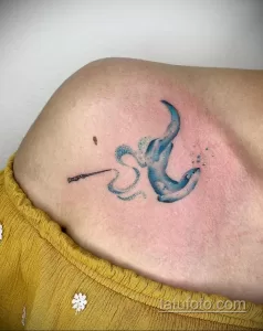 Фото акварельной татуировки тюленя, плывущего в воде на плече. Рисунок татуировки выполнен в нежных голубых и синих тонах.