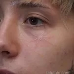 Фото тату: тонкая линия паука, расположенного рядом с глазом. Минималистичный эскиз тату для лица.