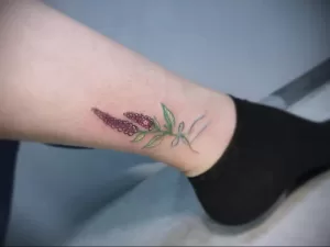 Фото тату: изящная татуировка с изображением соцветия лиловых цветов, выполненная в технике тонкой линии, расположена на запястье. Эскиз татуировки дополнен зелеными листьями.