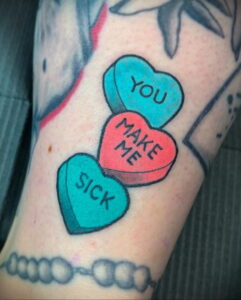 Фото тату: три конфетных сердечка с надписями "YOU", "MAKE", "ME SICK" на руке. Яркие цвета, стиль old school.