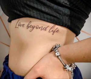 Фото татуировки с надписью "Love beyond life" на боку. Элегантная и романтичная татуировка, выполненная каллиграфическим шрифтом.
