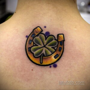 Фото тату подковы и четырехлистного клевера на спине. Яркий рисунок татуировки с использованием желтого, зеленого и фиолетового цветов.