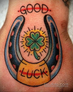 Фото татуировки подковы с четырехлистным клевером внутри и надписями 'Good Luck', выполненной в ярком традиционном стиле. Татуировка на руке.