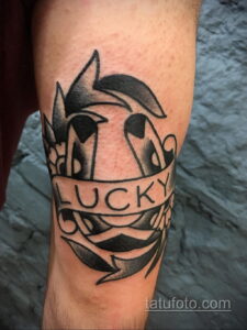 Фотография черно-белой татуировки подковы с надписью 'Lucky'. Простой дизайн, четкие линии, минималистичный стиль.
