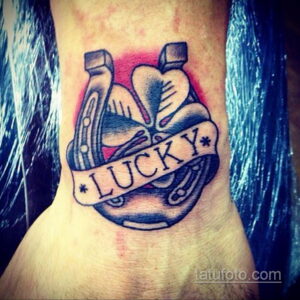 Фото тату подковы с надписью "LUCKY" на запястье. Черно-белый рисунок в стиле олдскул, символизирующий удачу и позитивный настрой.