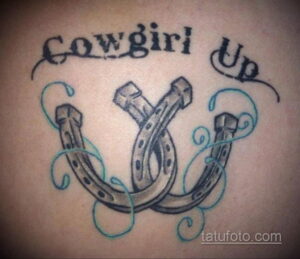 Фото тату подковы и надписи 'Cowgirl Up' в стиле графика. Черно-белый рисунок, четкие линии, татуировка на теле.