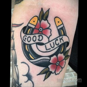 Фото тату подковы с надписью 'Good Luck' в стиле олд скул. Яркие цвета, четкие контуры, традиционный стиль, татуировка на руке.